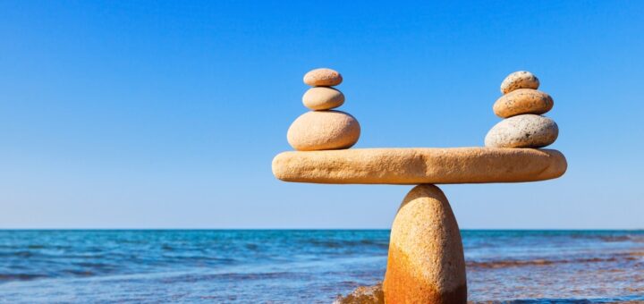 на фоні спокійного блакитного моря - кам'яні вагі, врівноважені маленькими камінчиками: хитка рівновага