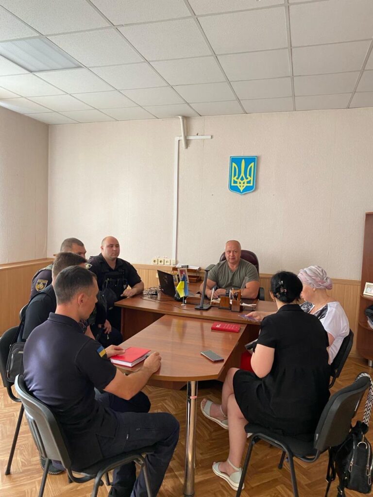 Засідання координаційного штабу Білозерської СВА. 06 червня 2023 року. Головує Михайло ЖАДАН, заступник начальника Херсонської РД(В)А. На фото: у світлій кімнаті за столом на засіданні сидять 7 людей: у голові столу — заступник начальника Херсонської РД(В)А Михайло ЖАДАН. Ліворуч від нього - 4 чоловіки у поліцейській формі, праворуч - 2 жінки