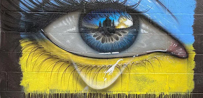 Стилізоване зображення на темній кам'яній стіні намальовано око зі сльозою у жовто-блакитних фарбах