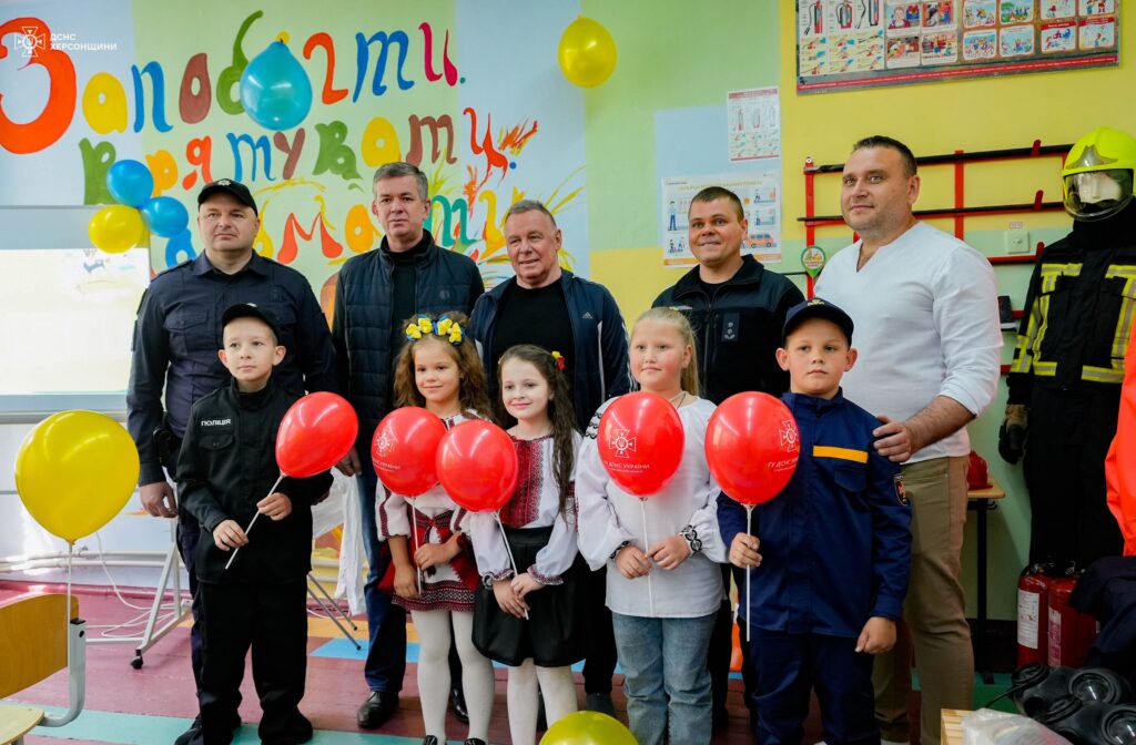 на передньому плані стоять маленькі школярі у вишиванках з червоними повітряними кульками, позаду них - співробітники національної поліції, голова райдержадміністрації Михайло ЛИнецький, голова ВА ТГ, директор навчального закладу з сином
