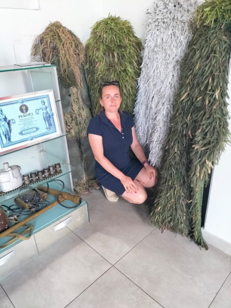 Співробітниця ХРД(В)А поруч з різноманітними військовими маскувальними сітками та стендом