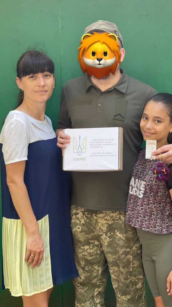 Військовий тримає коробку з сувеніром від співробітників ХРД(В)А, ліворуч від нього - співробітниця райадміністації, праворуч - всміхнена дівчинка