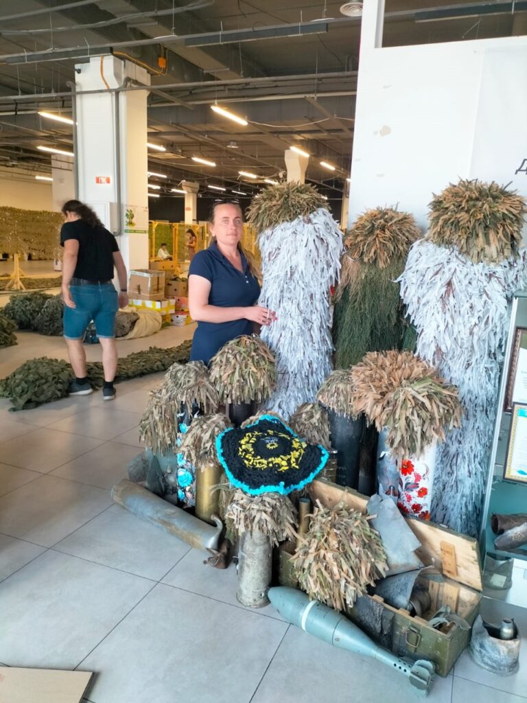 Співробітниця ХРД(В)А поруч з різноманітними військовими маскувальними сітками