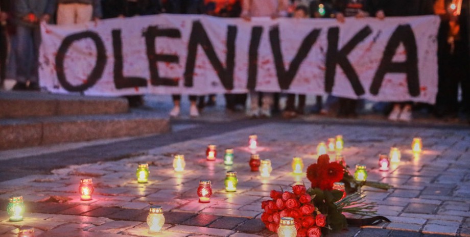 На білому плакаті з червоними плямами написано OLENIVKA, попереду плакату — запалені свічки та лампадки в пам'ять за загиблими Героями 
