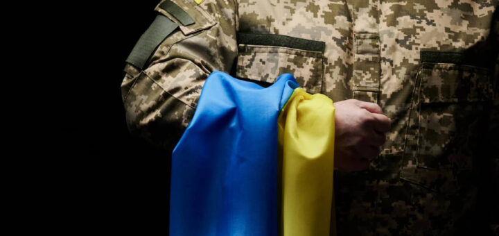 військовий тримає у руці жовто-блакитний прапор України