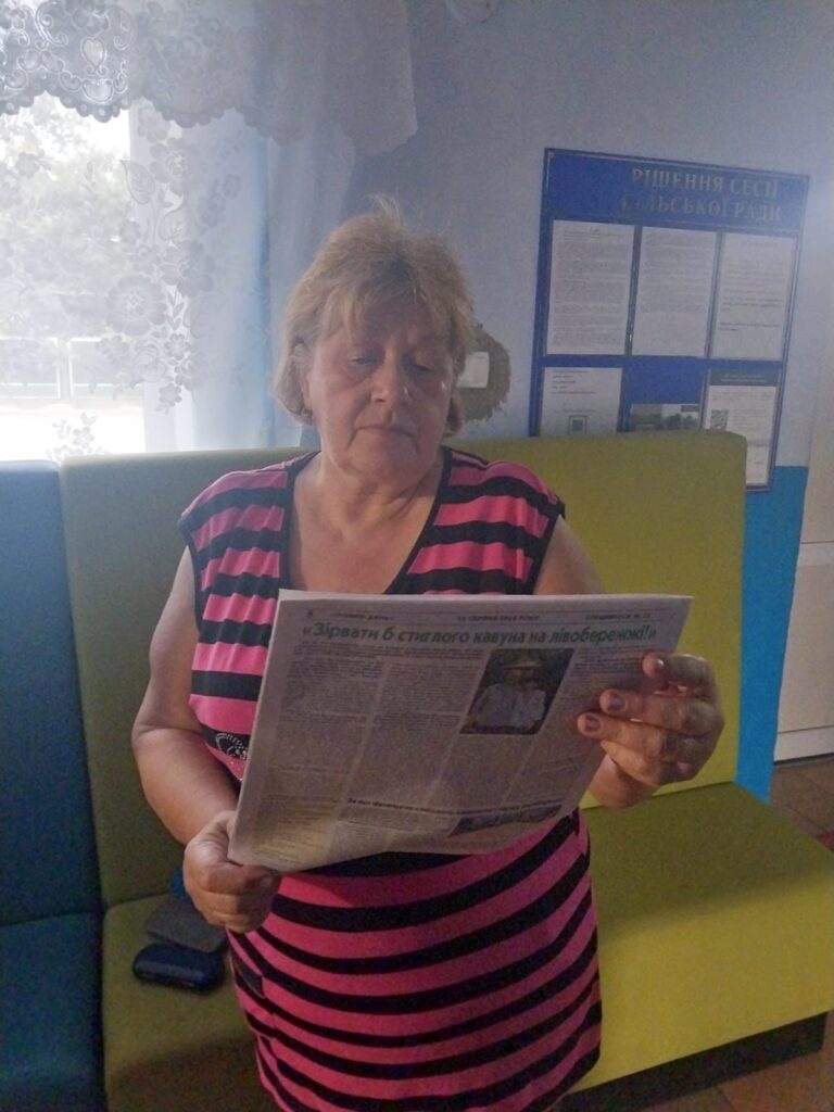 Жіночка у рожево-чорній смугастій сукні читає газету