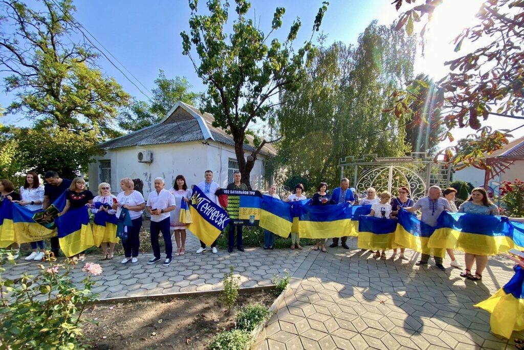 Багато людей на вулиці, що стоять довгою чергою, тримаючи великі прапори України