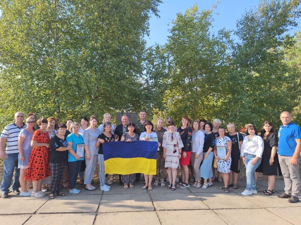 Багато всміхнених людей на площі з жовто-блакитним прапором України