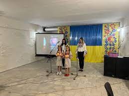 Маленькі дівчата в національних костюмах співають, позаду них - великий прапор України