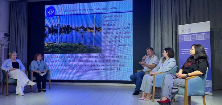 На сцені біля великого екрана сидять декілька жінок та чоловіків