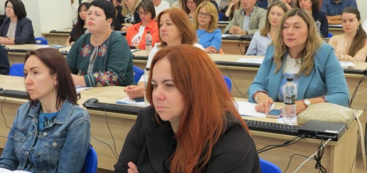 Багато слухачів сидять в аудиторії за столами та слухають лекцію