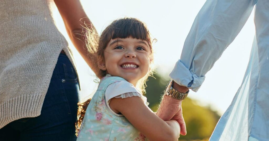 дівчинка тримає батьків за руки та всміхається