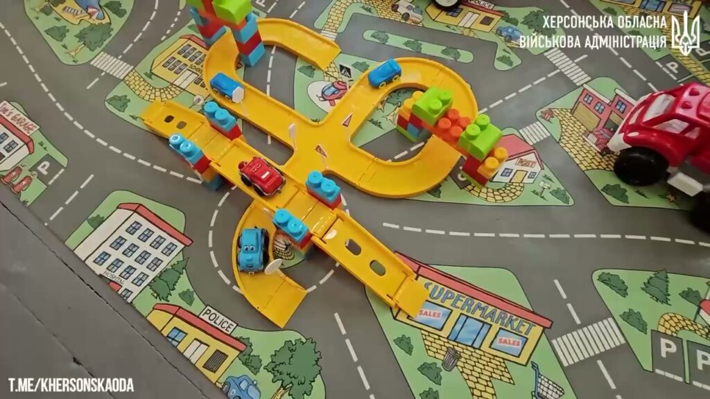 на столі - дитяча карта доріг, іграшковий міст з багатьма з'їздами та багато іграшкових різнокольорових машинок