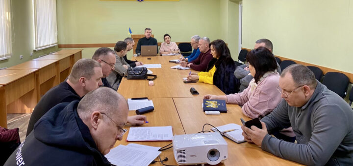 Начальники військових адміністрацій населених пунктів Херсонського району сидять у світлій кімнаті з гербом України за довгим столом, в голові столу — Михайло Линецький та Марина Малахова