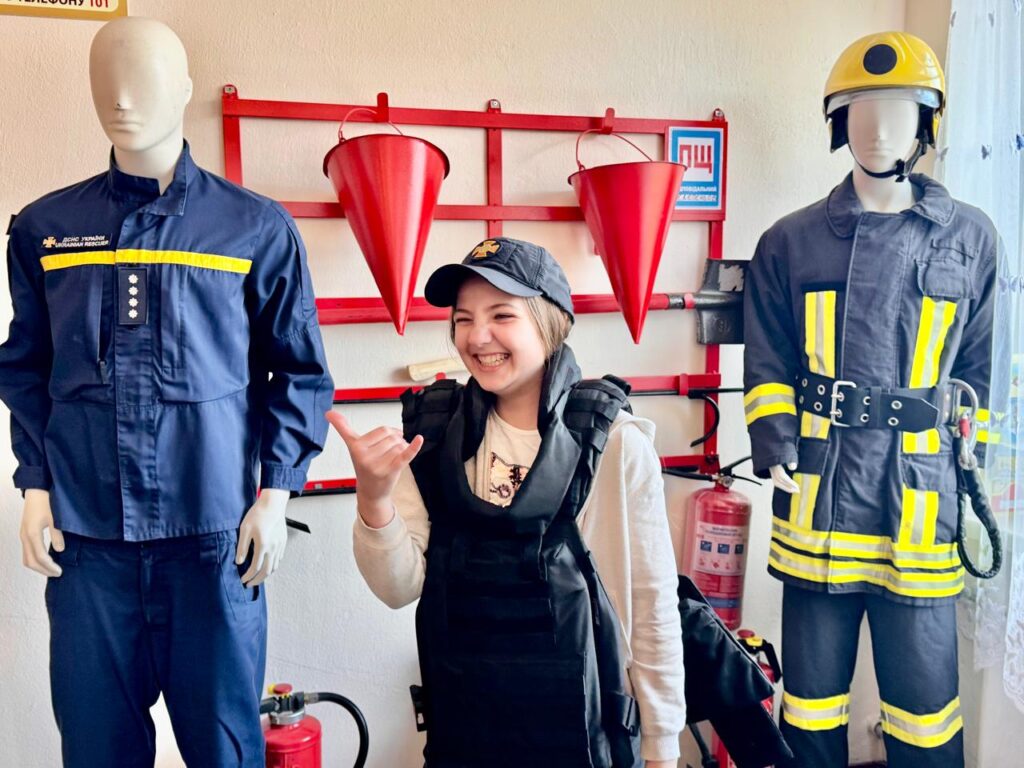 Всміхнена дівчина у бронежилеті у класі пожежної безпеки поруч з манекенами