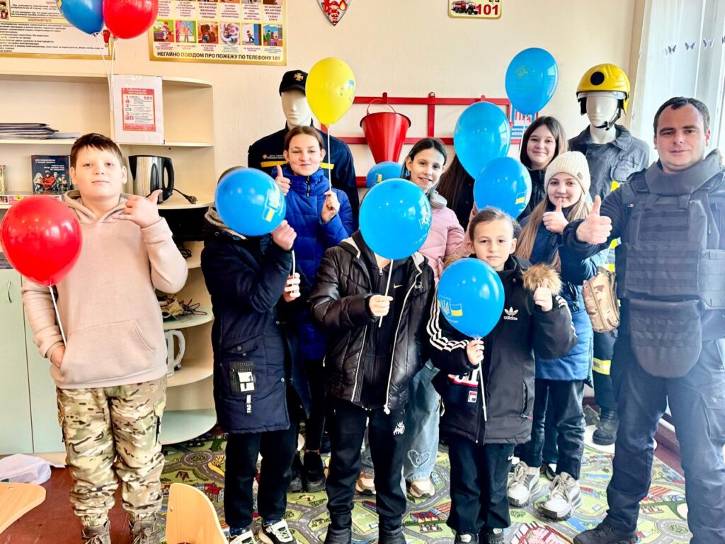 Діти з синіми повітряними кульками у класі пожежної безпеки поруч з рятувальником