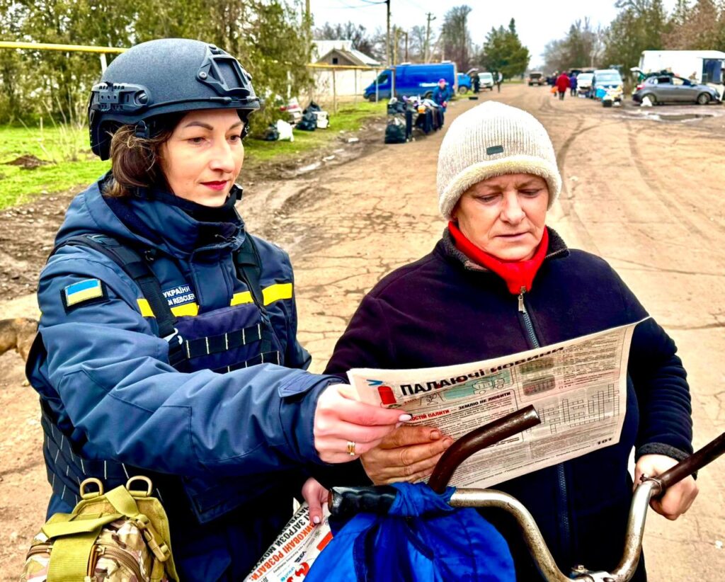 Працівниця поліції на вулиці показує жіночці з велосипедом газету