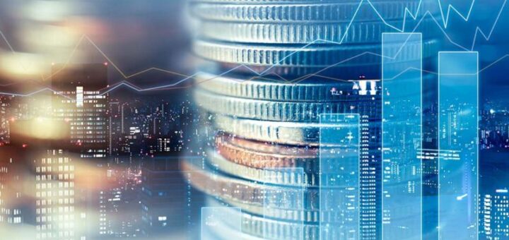 На зображенні стопка монет на передньому плані, складених одна на одну, з освітленим міським пейзажем та хмарочосами на задньому плані. Поверх накладені графіки й діаграми, що символізують фінансові ринки або економічні показники.