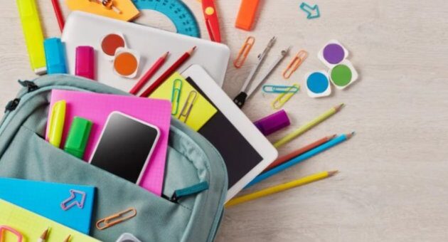 Рюкзак блакитного кольору зі шкільним приладдям: смартфон, планшет, блокнот, олівці, ручки, маркери, ножиці, циркуль, лінійка, клейкі нотатки й канцелярські дрібниці. Все лежить розсипом — сцена наче зібрана до навчання.