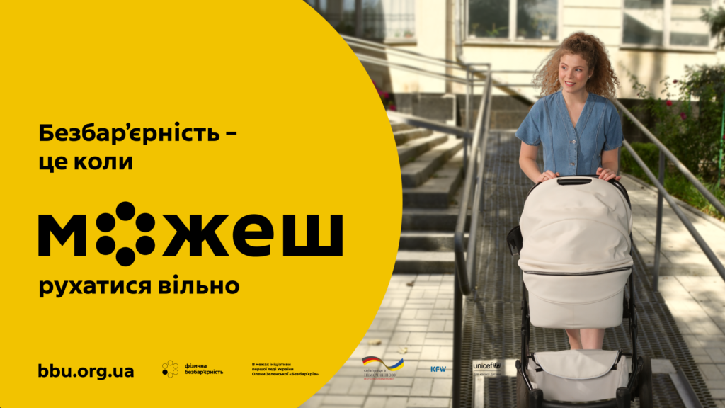 На фотографії зображено людину, яка стоїть на пандусі за дитячим візком. На тлі — будівля та зелена зона. На зображенні є текст українською: «Безбар’єрність – це коли м о ж е ш рухатися вільно». Нижче пояснення: «Фізична безбар’єрність передбачає, що будь-яка людина, незалежно від віку чи стану здоров’я, зможе користуватися навколишнім простором самостійно, без сторонньої допомоги