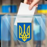  На зображенні — рука опускає бюлетень до прозорої виборчої урни з тризубом — гербом України. На фоні — сині та жовті штори, що символізують кольори українського прапора