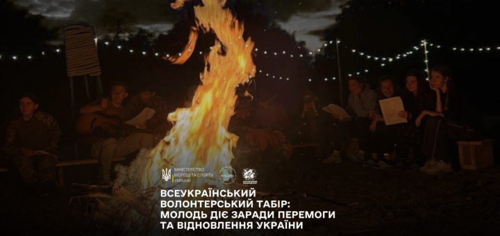 Група людей сидить навколо великого багаття вночі. Вогонь яскраво горить, освітлюючи простір. Деякі учасники тримають папери, один грає на гітарі. На фоні — дерева та гірлянди зі світлами, що створюють затишну атмосферу. Угорі — текст українською: «МІНІСТЕРСТВО МОЛОДІ ТА СПОРТУ УКРАЇНИ. ВСЕУКРАЇНСЬКИЙ ВОЛОНТЕРСЬКИЙ ТАБІР: МОЛОДЬ ДІЄ ЗАРАДИ ПЕРЕМОГИ ТА ВІДНОВЛЕННЯ УКРАЇНИ». Обстановка передає дух єдності, натхнення та активності молоді.