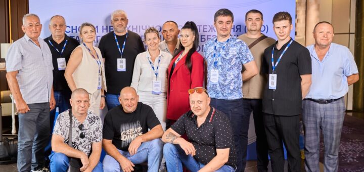 Усміхнені учасники стоять біля банера з логотипами Мінекономіки України, Demine Ukraine, ОБСЄ та Tetra Tech.