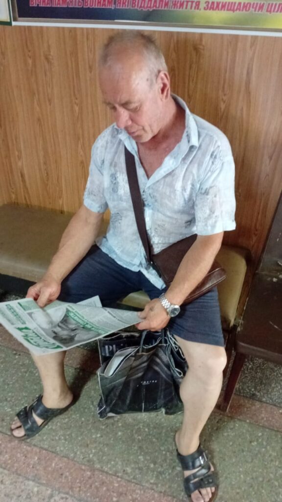 чоловік у білій сорочці сидить в приміщенні та читає газету "Гривна"