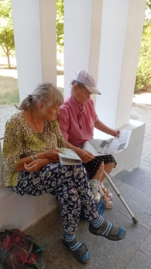 Дві жінки сидять на вулиці та читають газету