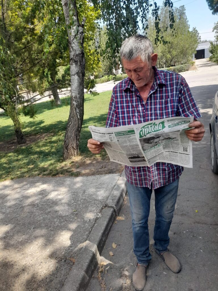 Чоловік на вулиці читає газету "Гривна"