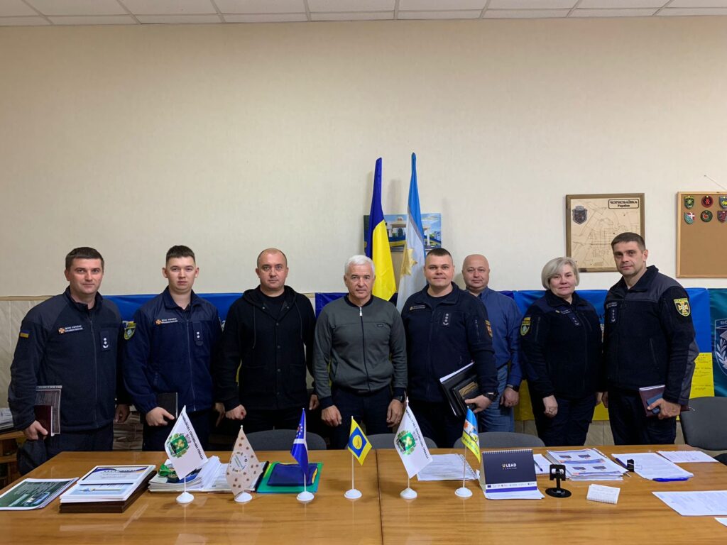 Вісім людей у формі стоять за конференційним столом у формальній обстановці. Позаду — прапори України та служби цивільного захисту, а також настінні емблеми