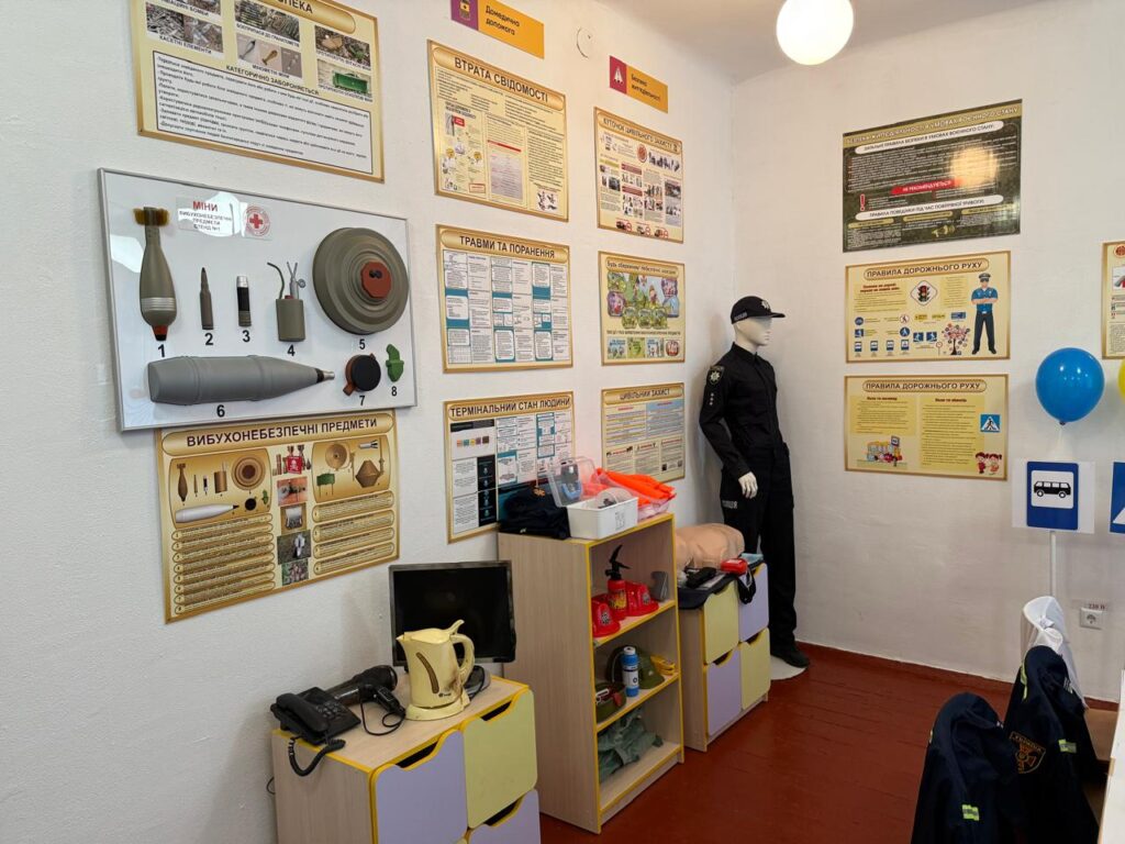 Кімната оформлена як навчальний простір із темою безпеки: на стінах — плакати з правилами поведінки при виявленні вибухонебезпечних предметів, а також стенд із макетами гранати, міни, снаряда, патрона та інших небезпечних об’єктів. Поруч — манекен у формі правоохоронця, полички з навчальними матеріалами та предметами, зокрема протигазом і каскою.