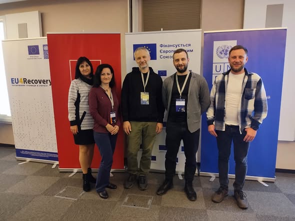 П’ятеро людей стоять у приміщенні перед трьома банерами. Лівий — «EU4Recovery» з логотипами ЄС і ПРООН. Центральний — напис «Фінансується Європейським Союзом». Правий — логотип ПРООН і текст українською.