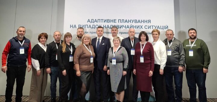 Тринадцять людей стоять перед банером із логотипами «ОТГ Асоціація» та «Партнерство за сильну Україну». Тема — адаптивне планування для прикордонних громад. Усі учасники — з бейджами, одяг — діловий.