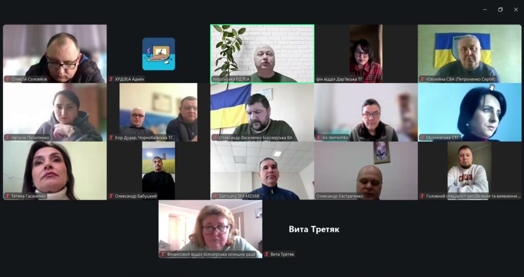 Скріншот Zoom-конференції з 17 учасниками. Більшість мають вимкнені мікрофони. У деяких кадрах — українські прапори, офіційні назви установ, зокрема: Херсонська РДА, Дар’ївська ТГ, Чорнобаївська ТГ, Білоцерська ВА, Музиківська СТГ. 