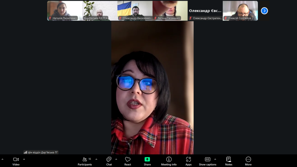 Скріншот Zoom-зустрічі, головний спікер — у червоній картатій сорочці, говорить у камеру. У відображенні окулярів — екран. Угорі — мініатюрні відео інших учасників, частина з вимкненими мікрофонами. Підпис головного спікера: «фін відділ Дар'ївська ТГ».
