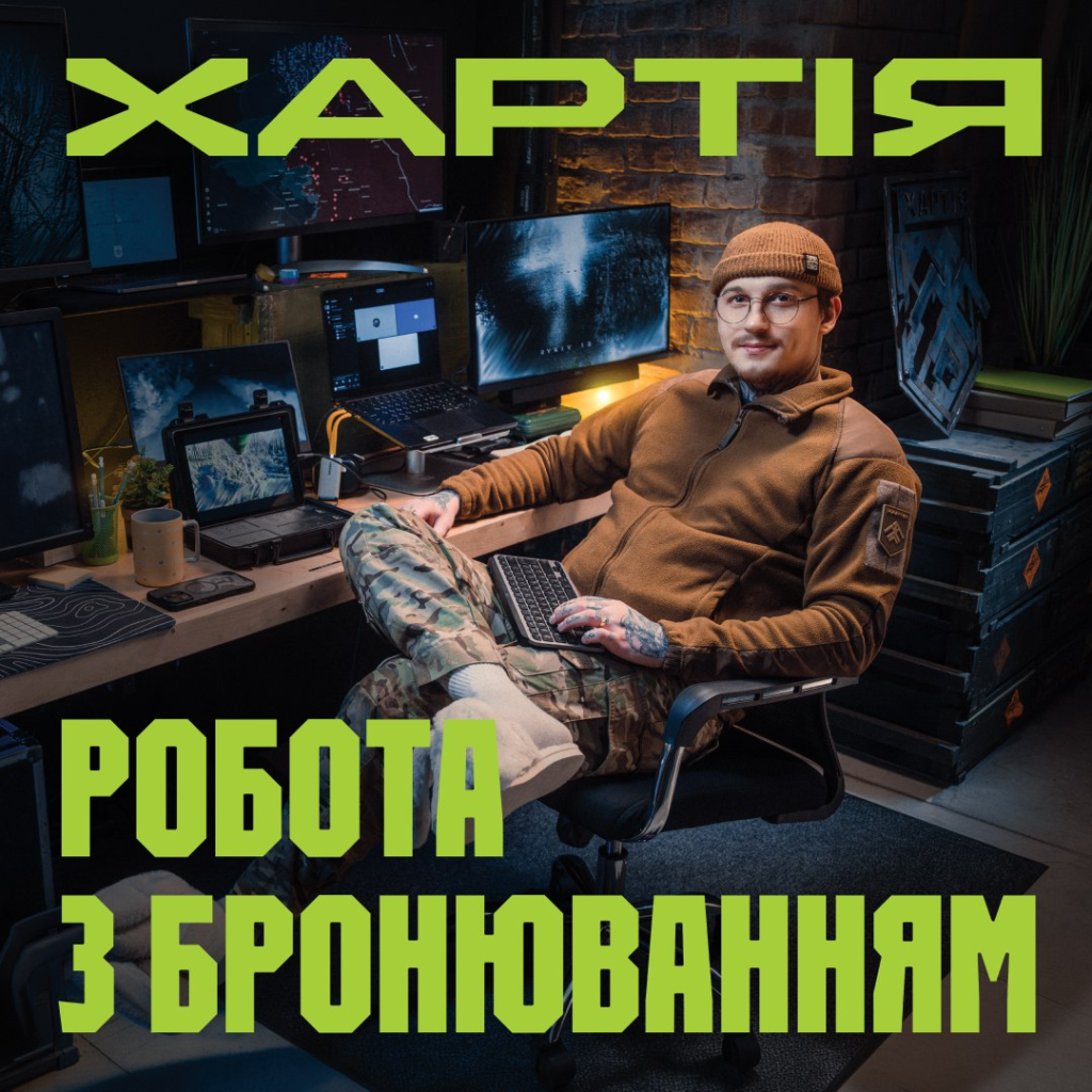 Людина у тактичному одязі працює за кількома моніторами у сучасному просторі, тримаючи клавіатуру