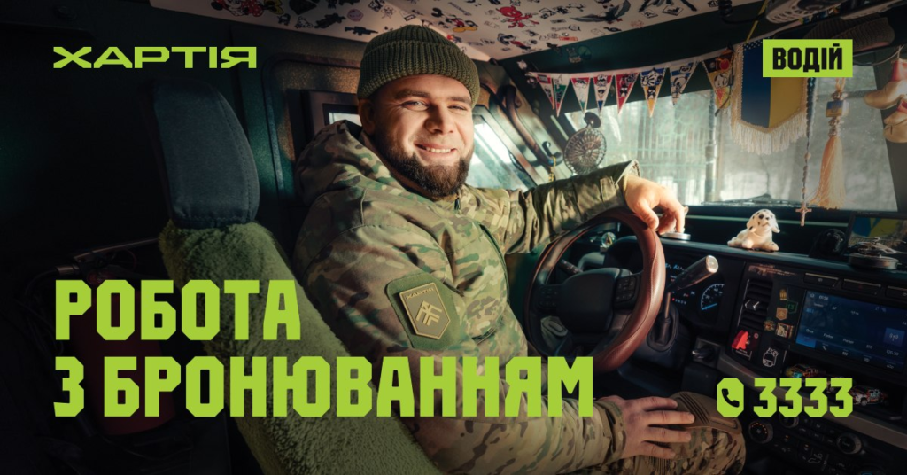 Військовий у камуфляжі сидить за кермом машини, усміхається, на панелі іграшка-собака та прикраси, текст українською: “Хартія. Водій. Робота з бронюванням. 📞 3333