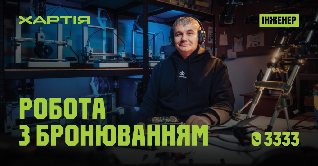 Чоловік у чорній худі з написом “Хартія” сидить у майстерні серед 3D‑принтерів та технічного обладнання, текст українською: “Інженер. Робота з бронюванням”