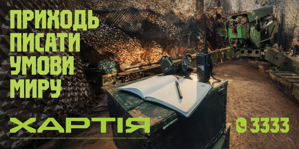 Військова сцена у бункері: зелена гармата, камуфляжна сітка, на металевій коробці лежать блокнот, ручка, навушники та рація. Текст українською: “Приходь писати умови миру. Хартія 3333”