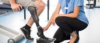 Людина з протезом ноги сидить на лавці, медичний працівник перевіряє та налаштовує протез