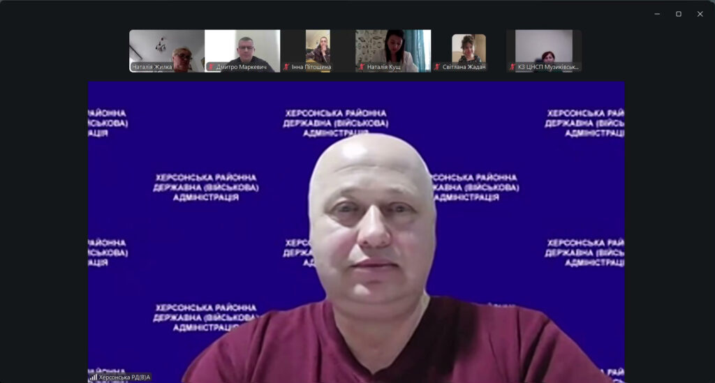Скріншот відеоконференції. У центрі — учасник у бордовій сорочці перед синім фоном із написом «Херсонська районна державна (військова) адміністрація». У верхній частині — маленькі віконця інших учасників із іменами