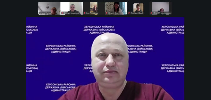Скріншот відеоконференції. У центрі — учасник у бордовій сорочці перед синім фоном із написом «Херсонська районна державна (військова) адміністрація». У верхній частині — маленькі віконця інших учасників із іменами