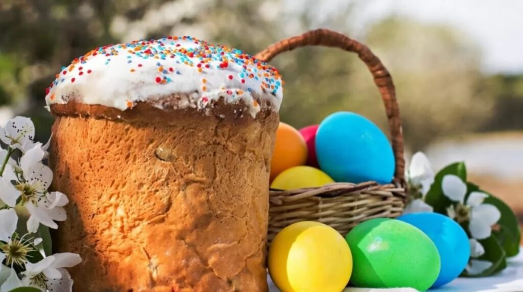 Великодній кошик із кольоровими писанками поруч із традиційною паскою з білою глазур’ю та посипкою