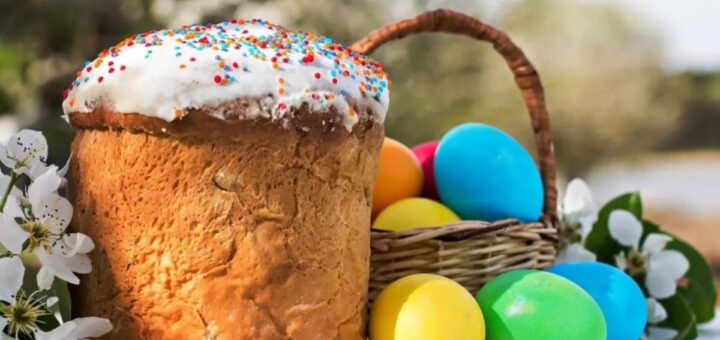 Великодній кошик із кольоровими писанками поруч із традиційною паскою з білою глазур’ю та посипкою