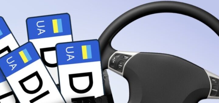 Кермо автомобіля праворуч, ліворуч кілька українських номерних знаків із позначкою UA та літерами DL