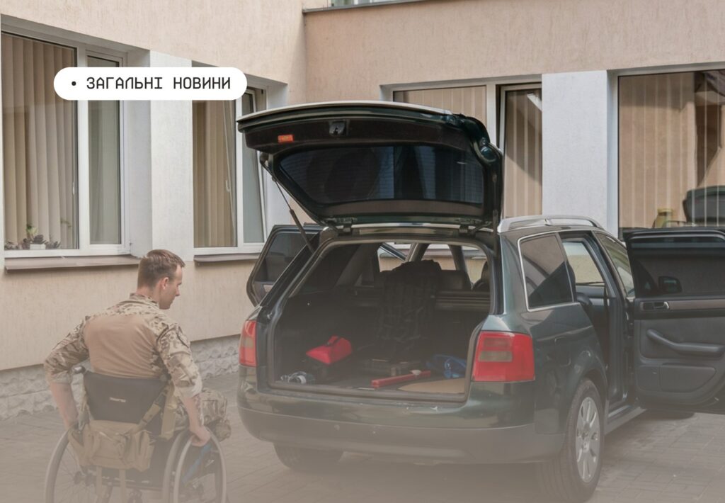 Людина у візку біля відкритого багажника зеленого універсала, поруч інструменти та речі