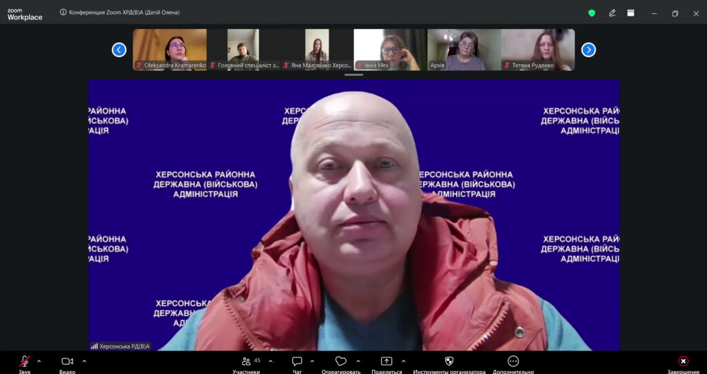 У центрі Михайло Анатолійович Жадан у червоній куртці та синій сорочці перед синім фоном із написом «Херсонська районна державна (військова) адміністрація». У верхній частині — маленькі віконця інших учасників у різних кімнатах.