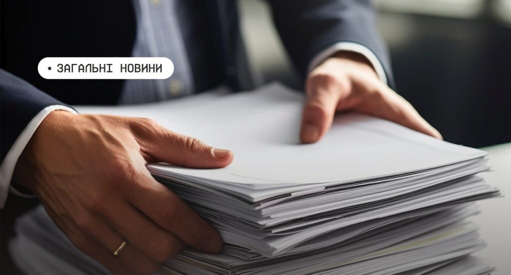 Людина в костюмі переглядає та впорядковує велику стопку документів на столі; текст “Загальні новини