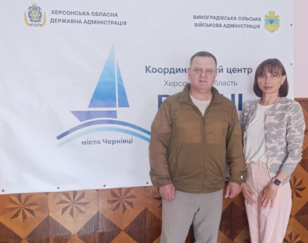 Начальник Служби у справах дітей Херсонської районної державної адміністрації Євгенія Степанська та начальника Виноградівської сільської військової адміністрації Валерій Мельниченко під час робочої зустрічі, стоять біля плакату «Вільні разом» у місті Чернівці